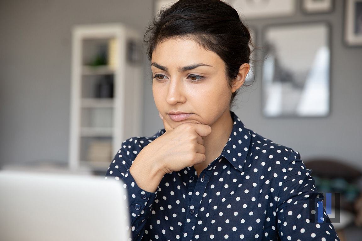 Unsure Indian business woman sit at desk looks at laptop screen thinking over task do research analyzing results feels doubtful